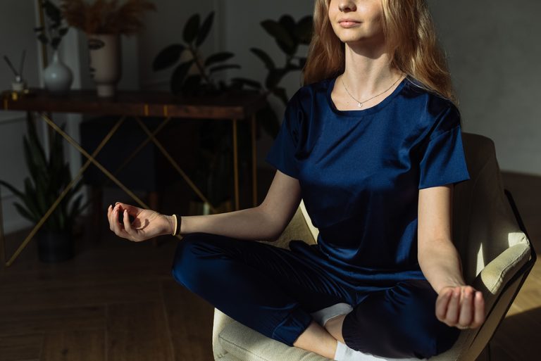 A young woman in recovery meditating on an armchair at home.
