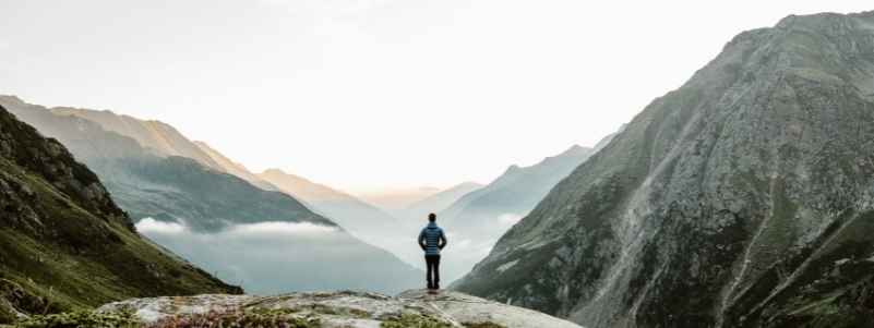 A hiker stops to look at the mountains that rise above the cloud line