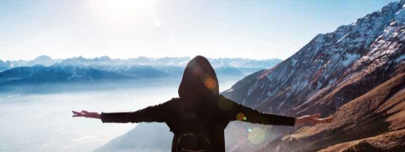 A person with their arms outstretched overlooking a mountain range
