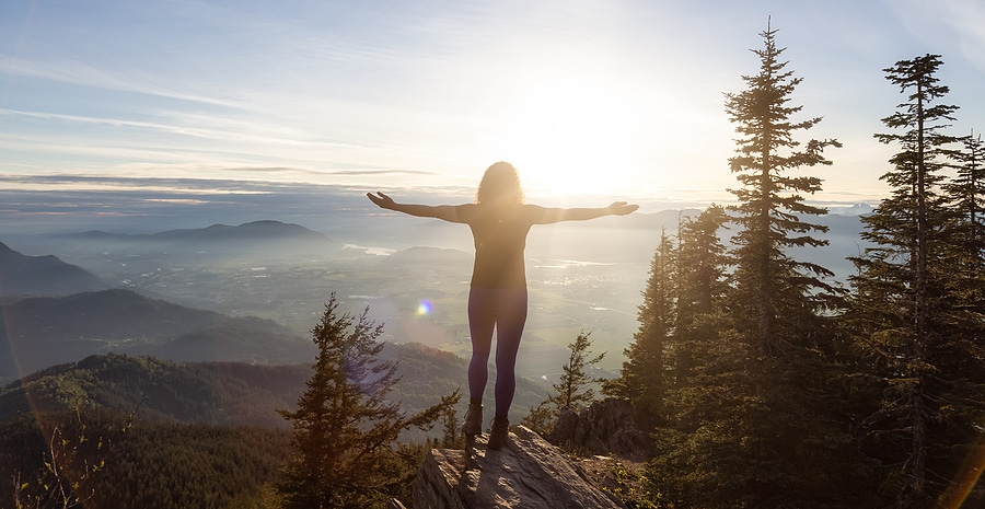 Woman holding her hands wide in a photo of her at a vista point in a mountain range