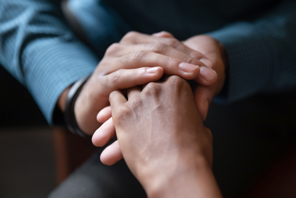 Close up photo of holding hands in a comforting manner